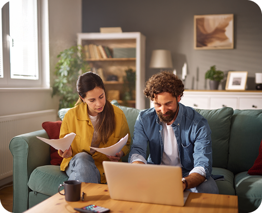 A couple sitting on a sofa with a laptop and paperwork