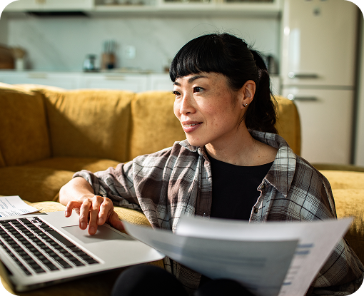 A person working at a laptop on a sofa with documents