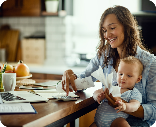 A parent holding a baby while working at a laptop