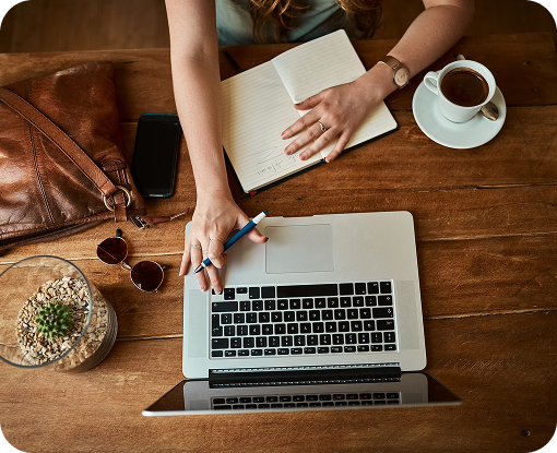Overhead view of a person writing in a notebook beside a laptop and coffee