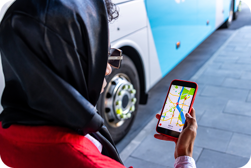 A person in a red headscarf checking a map on their phone beside a bus