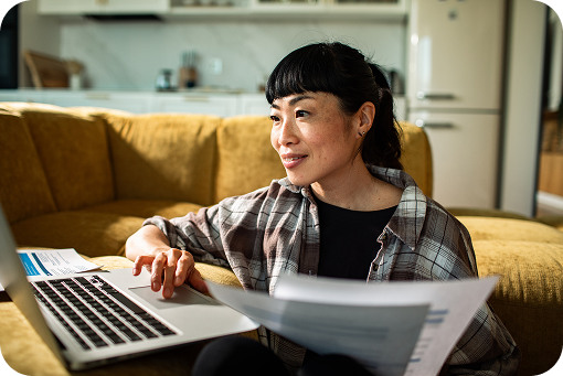 A person working at a laptop on a sofa with documents