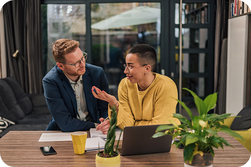 Two colleagues talking over a laptop at a table with plants