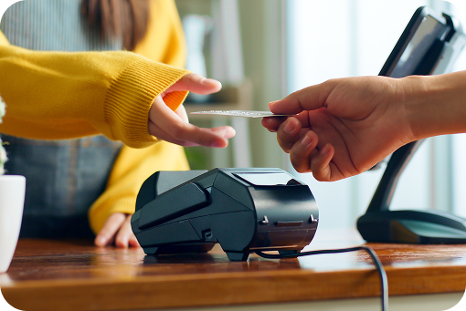 A hand passing a payment card to a cashier at a terminal