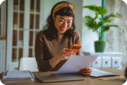 A person reading a document at a desk beside a laptop