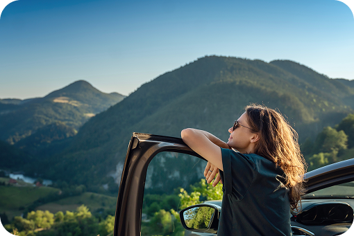 A person standing beside a car looking out at mountains