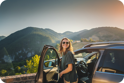A traveller standing beside a car with mountains behind