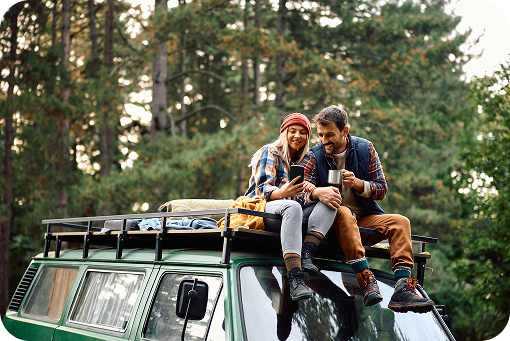 A group sitting on the roof of a camper van in a forest
