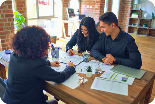 A group meeting around a table with documents and laptops