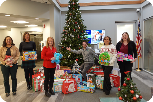 Waypoint staff standing with donated gifts beside a Christmas tree in a branch lobby