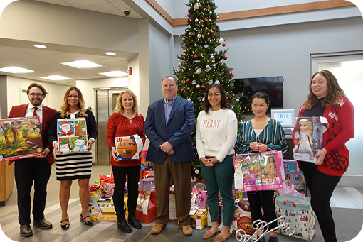 Waypoint staff holding donated gifts beside a Christmas tree in a branch lobby