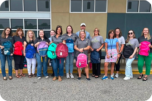 A large group of volunteers standing outdoors with donated backpacks