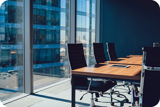 An empty boardroom with chairs along a long table beside tall windows
