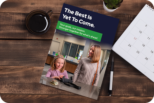 A printed annual report on a wooden desk beside a coffee cup and notepad